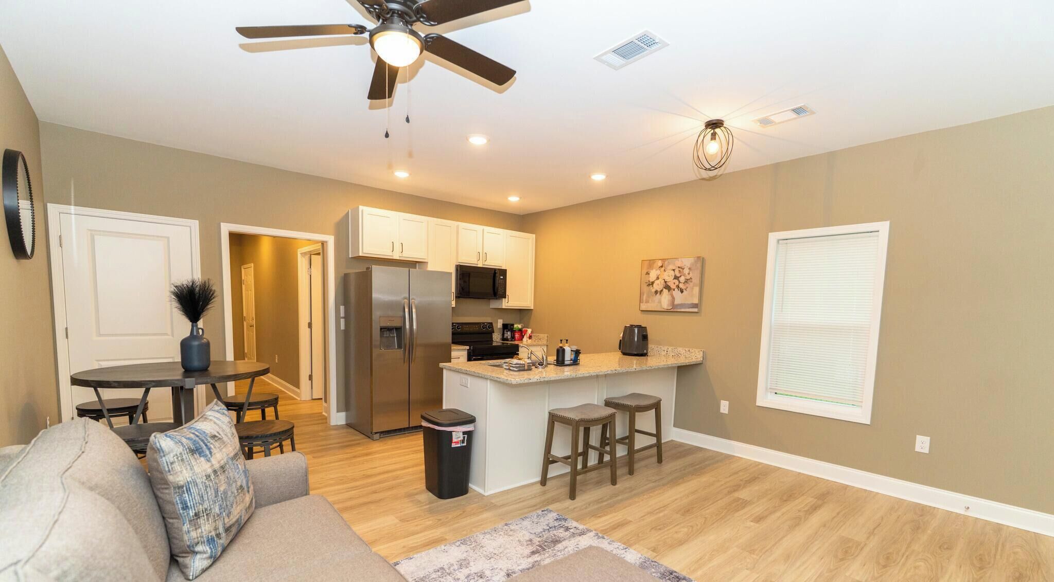 A modern kitchen with a central island, a dining area with a round table, and a ceiling fan.
