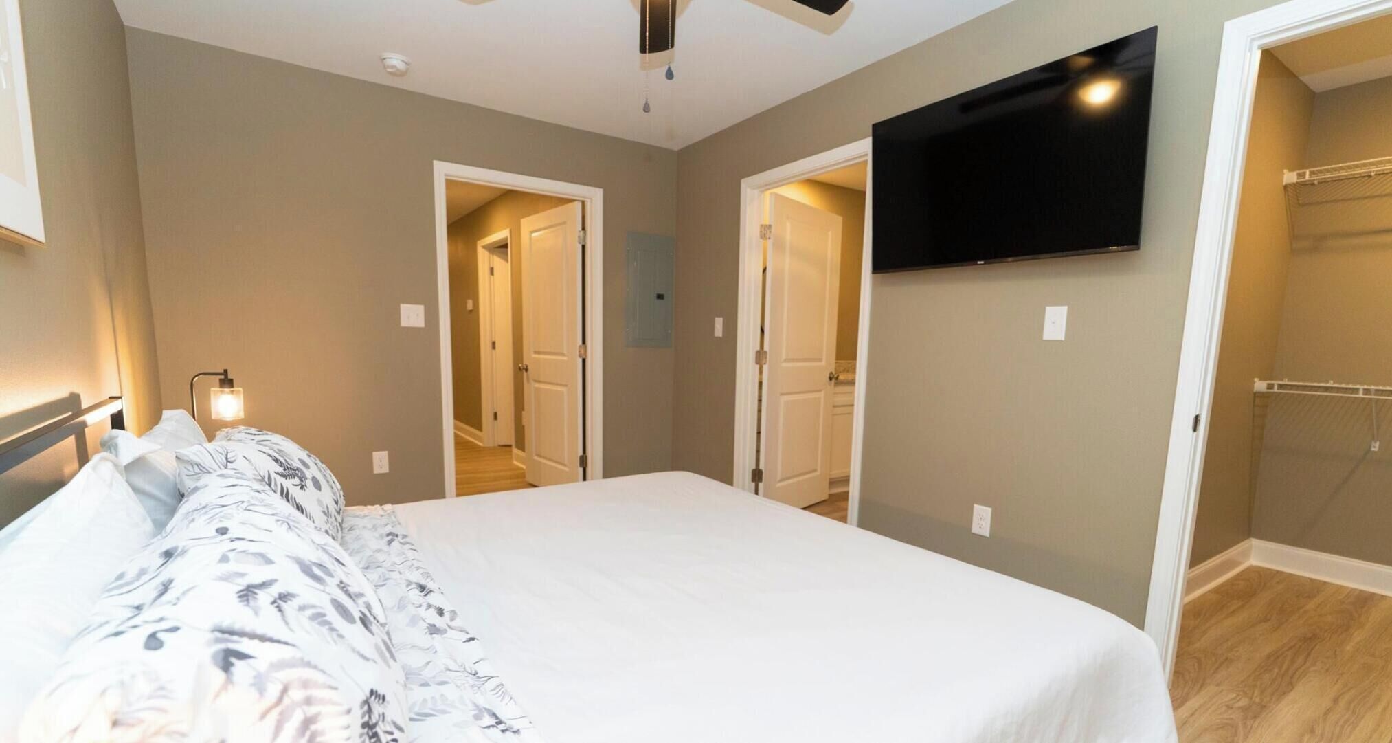 Un dormitorio con cama, televisor montado en la pared y vestidor.