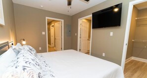 A bedroom with a bed, a TV mounted on the wall, and a walk-in closet.
