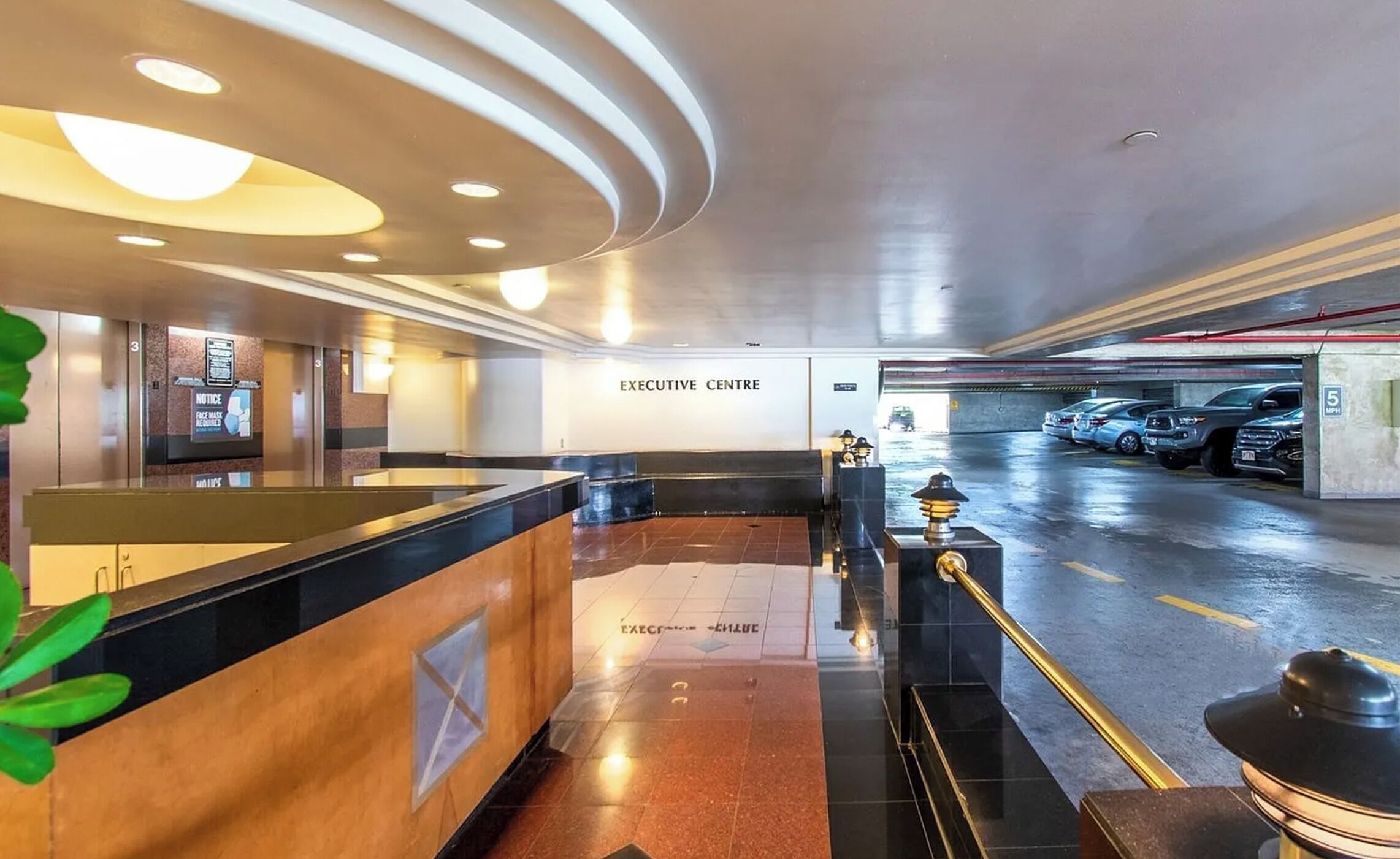 An executive center with a reception desk, a notice board, and a parking area with cars.