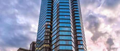 A tall, modern skyscraper with a reflective glass facade, surrounded by urban buildings and street lights.