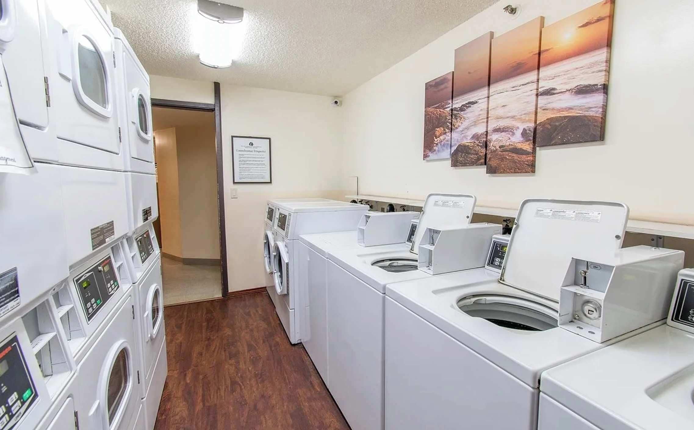 Un lavadero con varias lavadoras, piso de madera y una pared decorada con tres cuadros.