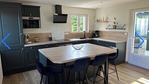 Cozinha moderna com ilha central, banquetas e uma grande janela que proporciona luz natural.
