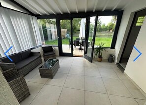 Ein überdachter Patio-Bereich mit einer Couch, einem Couchtisch und einem Esstisch.