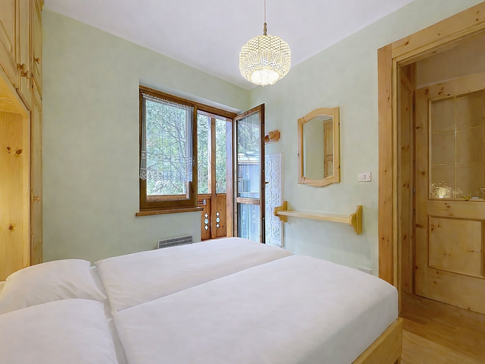 A bedroom with a bed, a window, a mirror, and a door.