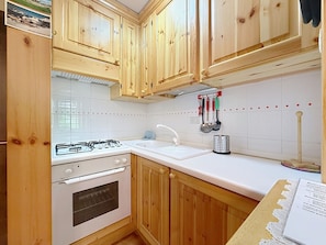 A kitchen with wooden cabinets, a gas stove, a sink, and hanging utensils. - Apartment Anny by Interhome (Canazei)