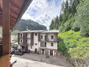 A two-story building with balconies, a parking area, and a mountainous backdrop. - Apartment Anny by Interhome (Canazei)