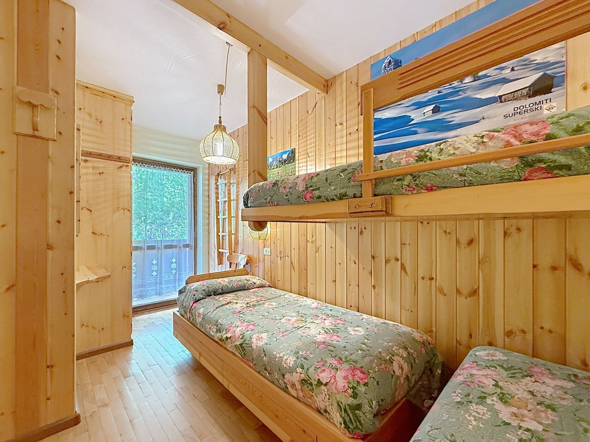 L’intérieur d’une cabane en bois, avec un lit superposé, une échelle, un luminaire suspendu et un tableau représentant un paysage enneigé.
