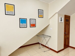 Un pasillo con un tendedero de metal, una puerta de madera y cuatro cuadros abstractos en la pared.