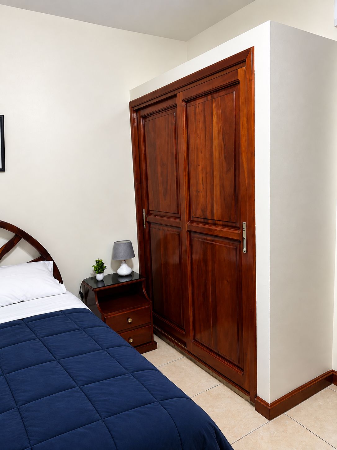Une chambre à coucher avec un lit, une table de chevet, une lampe et une armoire en bois.