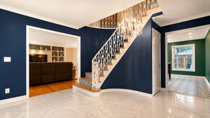 A modern interior with a marble floor, a staircase with a unique design, and a view of a green room through a doorway.