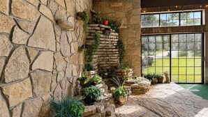 A stone wall with a built-in fireplace, potted plants, and a view through a large window.