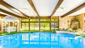 An indoor swimming pool with a wooden deck, large windows, and a stone wall.