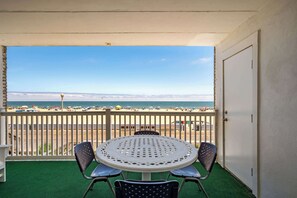 A balcony with a view of the beach, a round table with chairs, and a door. - Direct Oceanfront Condo on Ocean City’s Boardwalk (Ocean City)