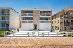 A multi-story residential building with balconies, a wooden deck in front, and a clear sky. - Direct Oceanfront Condo on Ocean City’s Boardwalk (Ocean City)