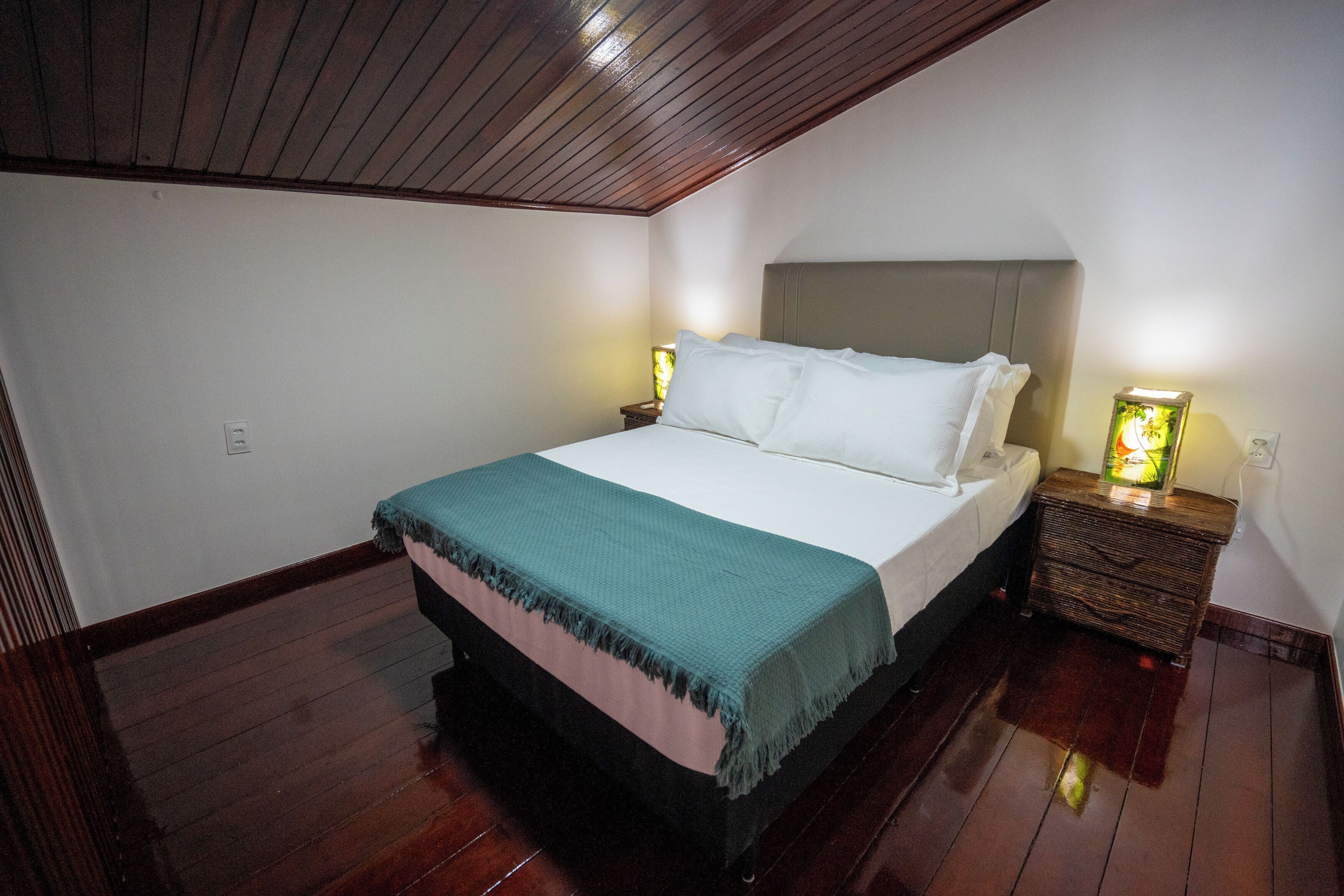 Un dormitorio con cama, cabecero de madera, mesitas de noche y una mesita de noche con lámpara.
