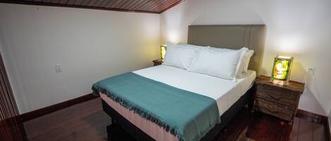Un dormitorio con cama, cabecero de madera, mesitas de noche y una mesita de noche con lámpara.