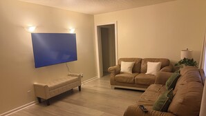 Olohuoneessa on seinälle asennettu taulutelevisio, vaaleanbeige sohva ja ruskea nahkasohva.