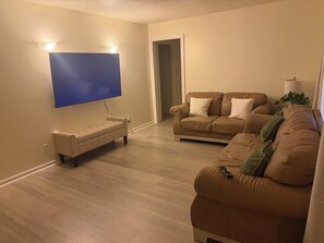 Ein Wohnzimmer mit einem an der Wand befestigten Flachbildfernseher, einem beige-farbenen Sofa und einem braunen Ledersofa.