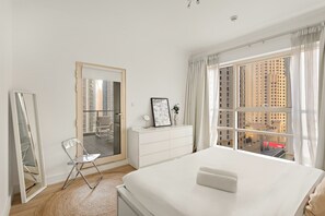 Ein Schlafzimmer mit einem Bett, einer Kommode, einem Stuhl, einem Spiegel und einem großen Fenster mit Blick auf die Stadt.