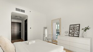Ett modernt hotellrum med en säng, en byrå, en spegel och ett fönster med utsikt över staden.
