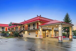 Un motel de dos pisos con techo rojo y estacionamiento cubierto.