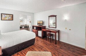 Una habitación de hotel con cama, escritorio, silla, televisor y espejo.