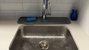 Una lavandino da cucina con un rubinetto, una spugna blu e un vaso azzurro sul piano di lavoro.