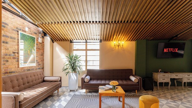 Ein möbliertes Wohnzimmer mit einer Couch, einem Couchtisch, einer Topfpflanze, einem an der Wand montierten Fernseher und einem karierten Boden.