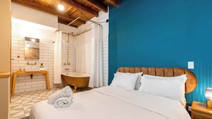 Ein Hotelzimmer mit einem Bett, einem hölzernen Kopfteil, einem Nachttisch, einem Badezimmer mit einer Badewanne und einer blauen Akzentwand.