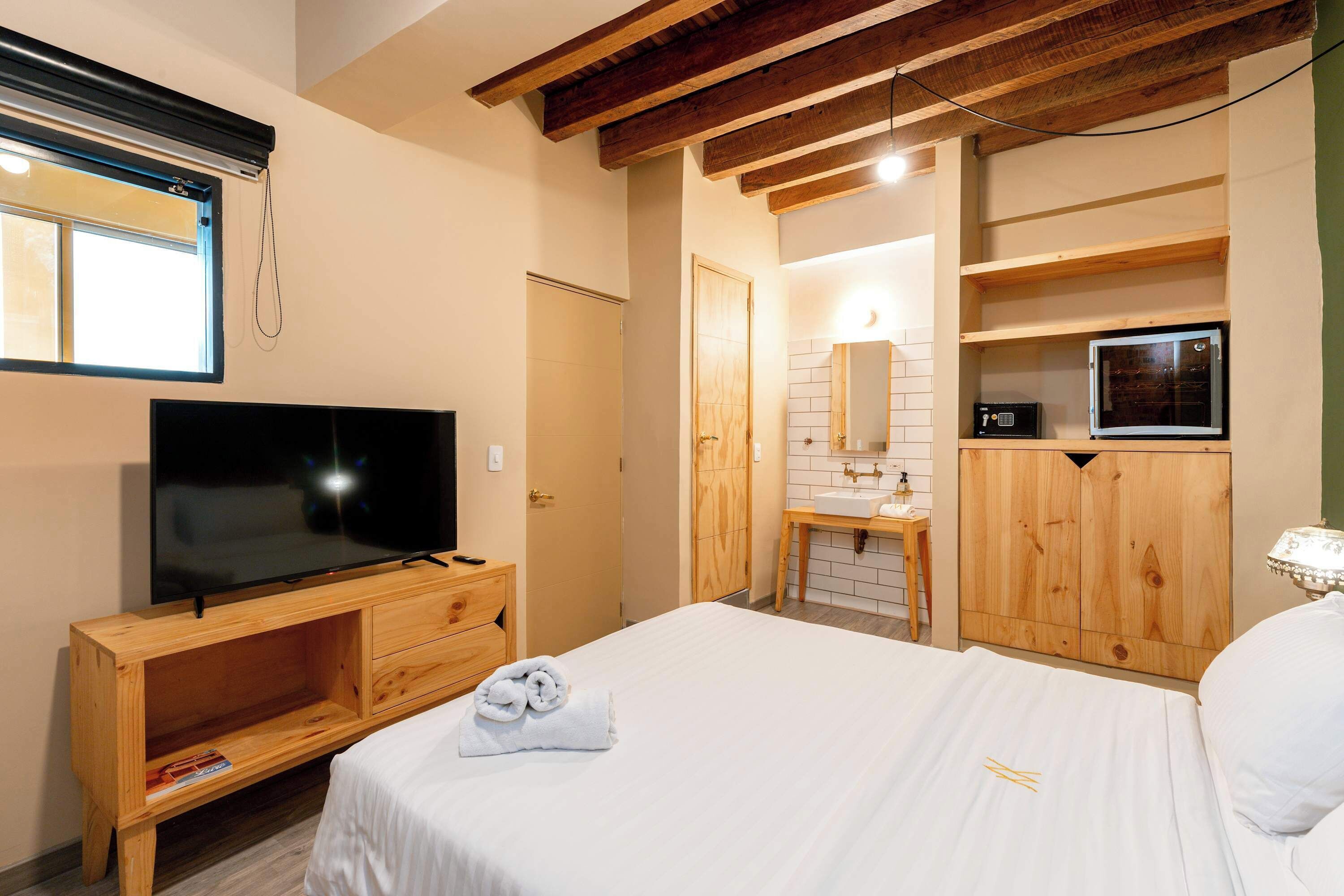A bedroom with a TV, wooden furniture, a bed, a bathroom with a mirror, and a wooden cabinet.