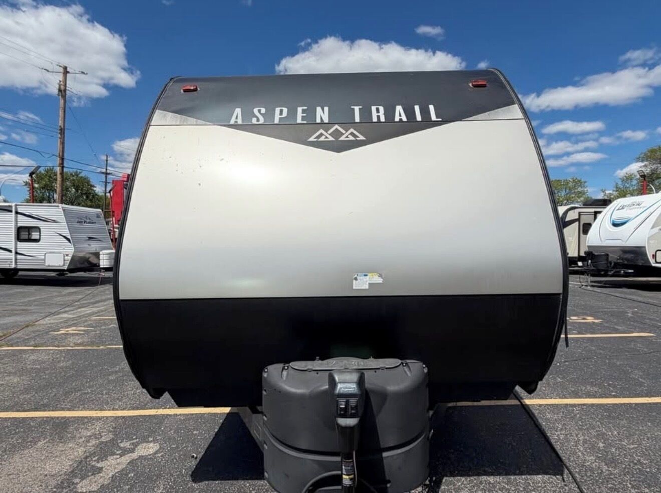 A large, cylindrical RV with 'ASPEN TRAIL' branding, a smaller attached unit, and a visible control panel.