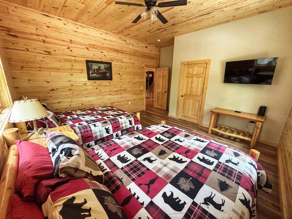 Ein Zimmer in einer Holzhütte mit zwei Betten, einem Deckenventilator, einem Fernseher und einer Holzbank.