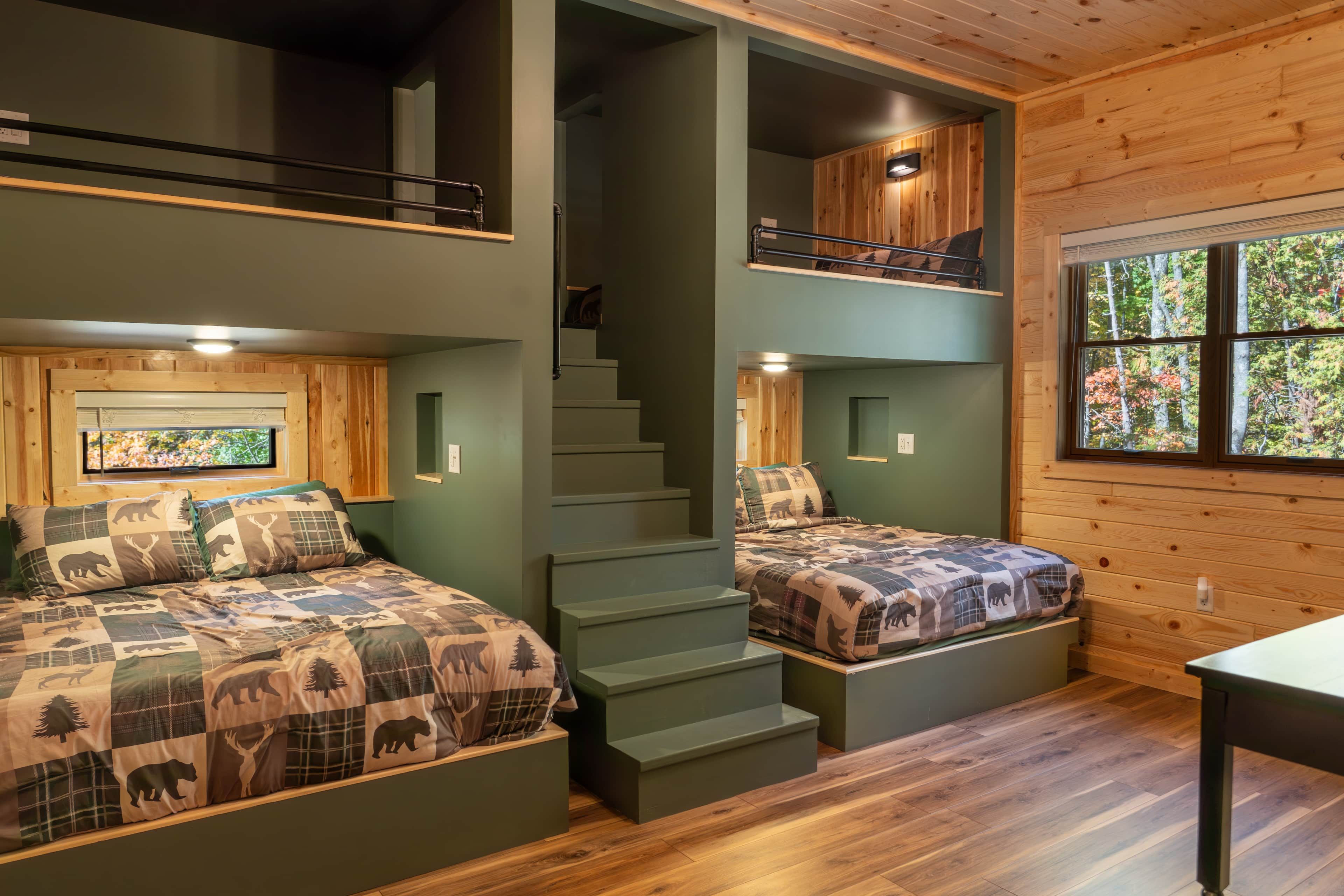 Una cabaña con dos habitaciones, cada una con una cama y un edredón con motivos de fauna, una escalera que conecta los pisos y un ventanal con vista a árboles.