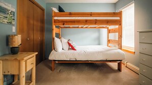 Ein Stockbett mit Holzrahmen, ein Nachttisch mit Lampe sowie eine Kommode mit Schubladen.