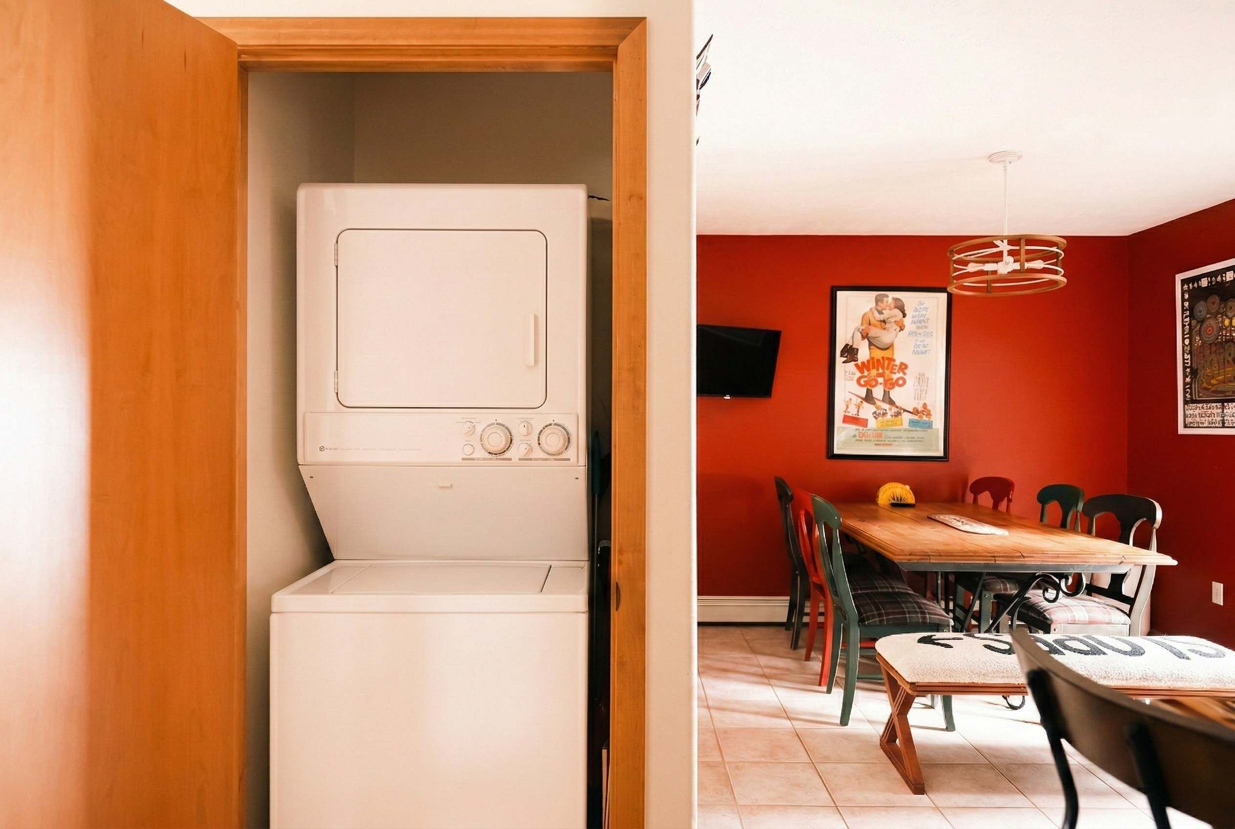 A compact kitchen with a built-in washer and dryer, a dining area with a wooden table and chairs, and red walls.