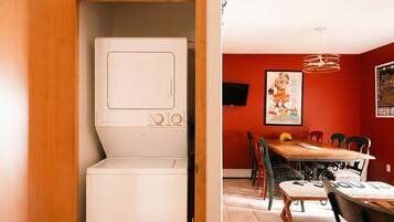 A compact kitchen with a built-in washer and dryer, a dining area with a wooden table and chairs, and red walls.