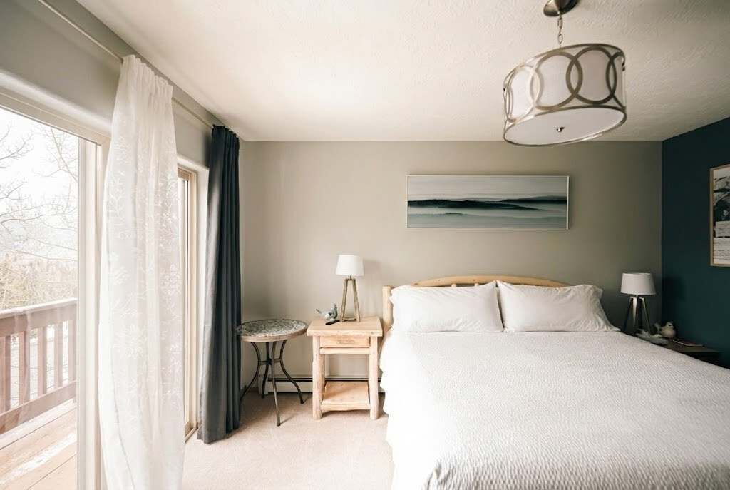 A bedroom with a bed, bedside tables, a nightstand, a window with curtains, and a ceiling light fixture.