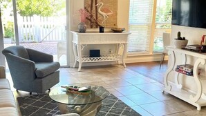 A living room with a ceiling fan, a glass coffee table, a grey armchair, a white console table, and a flat-screen TV mounted on the wall. - Sunny Sarasota Escape/ Minutes away from Siesta Key & Downtown (Sarasota)