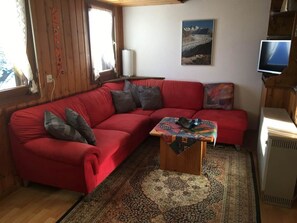 A red sofa with cushions, a patterned rug, a small wooden table, a painting on the wall, and a television on a stand. - Almenrausch 2. OG Süd-Ost Appartement/Fewo, Dusche und Bad, WC by Interhome (Riederalp)