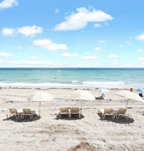 A beach with three umbrella-covered seating areas and a clear view of the ocean. - SLEEPS 8! Beautiful & Inviting 1-BR + 1.5-BA Condo On The Beach  (Hollywood)
