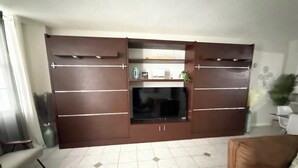 Ein Wohnzimmer mit einem großen Flachbildfernseher an einer holzverkleideten Unterhaltungseinheit, einem Sofa und einem Couchtisch.