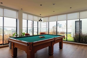 A pool table in a room with large windows, wooden flooring, and a hanging light fixture. - w* | Enchanting 2BR w/ Balcony in Miraflores (Miraflores)