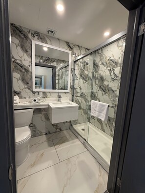 A modern bathroom with a marble backsplash, a large mirror, a sink, a toilet, and a glass-enclosed shower. - Skylux Hotel Long Island City (Long Island City)
