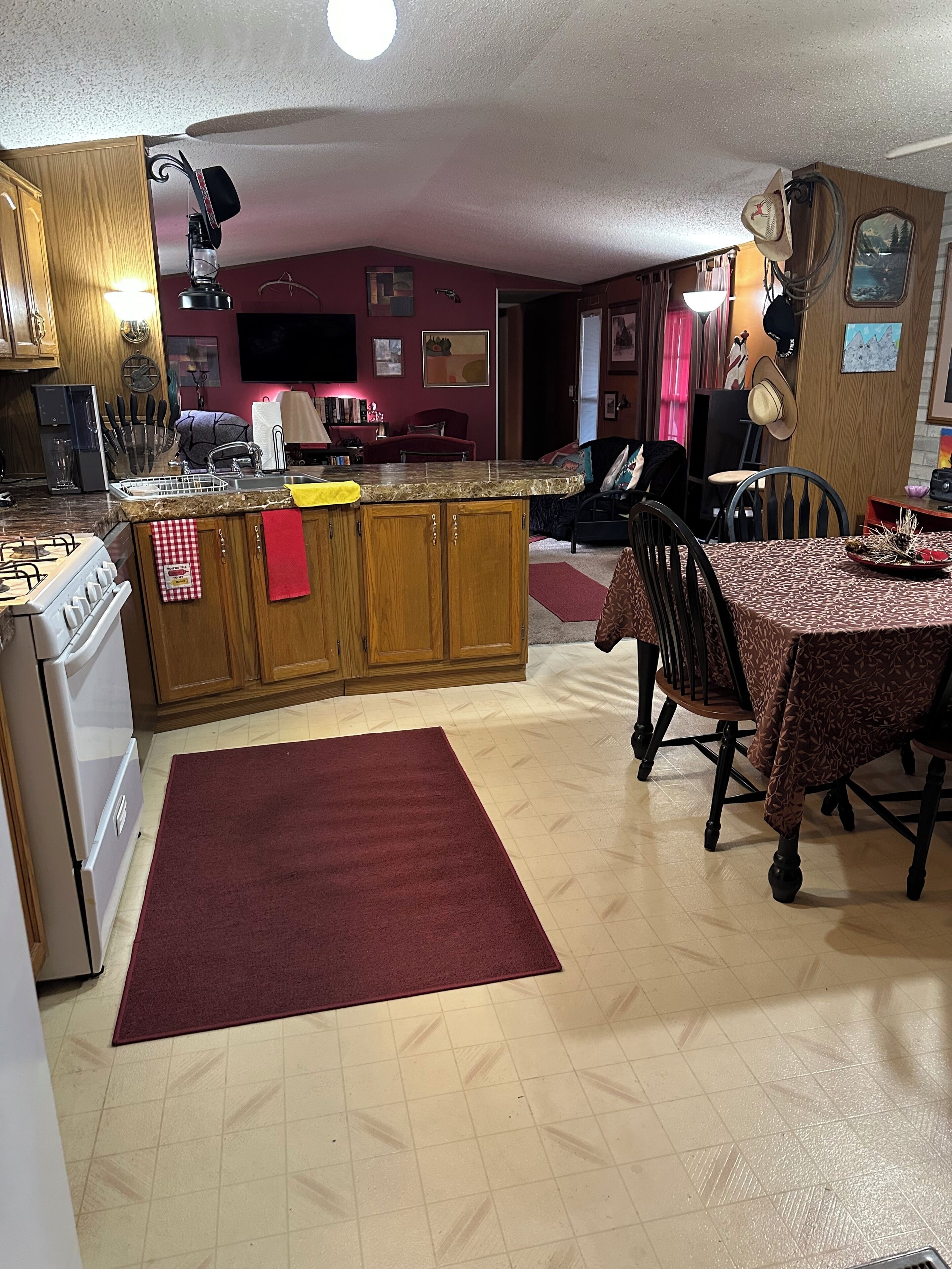 Una cocina con armarios de madera, una estufa a gas, una mesa de comedor con sillas y una alfombra roja.