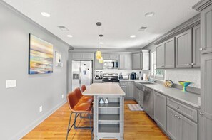 A modern kitchen with a central island, gray cabinetry, and a hanging pendant light. - A place to Wine Down in Cherry Grove! Pool, Hot Tub & Optional Golf Cart (Atlantic Beach)