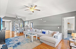 A spacious living room with a large sectional sofa, a glass coffee table, and a ceiling fan. - A place to Wine Down in Cherry Grove! Pool, Hot Tub & Optional Golf Cart (Atlantic Beach)
