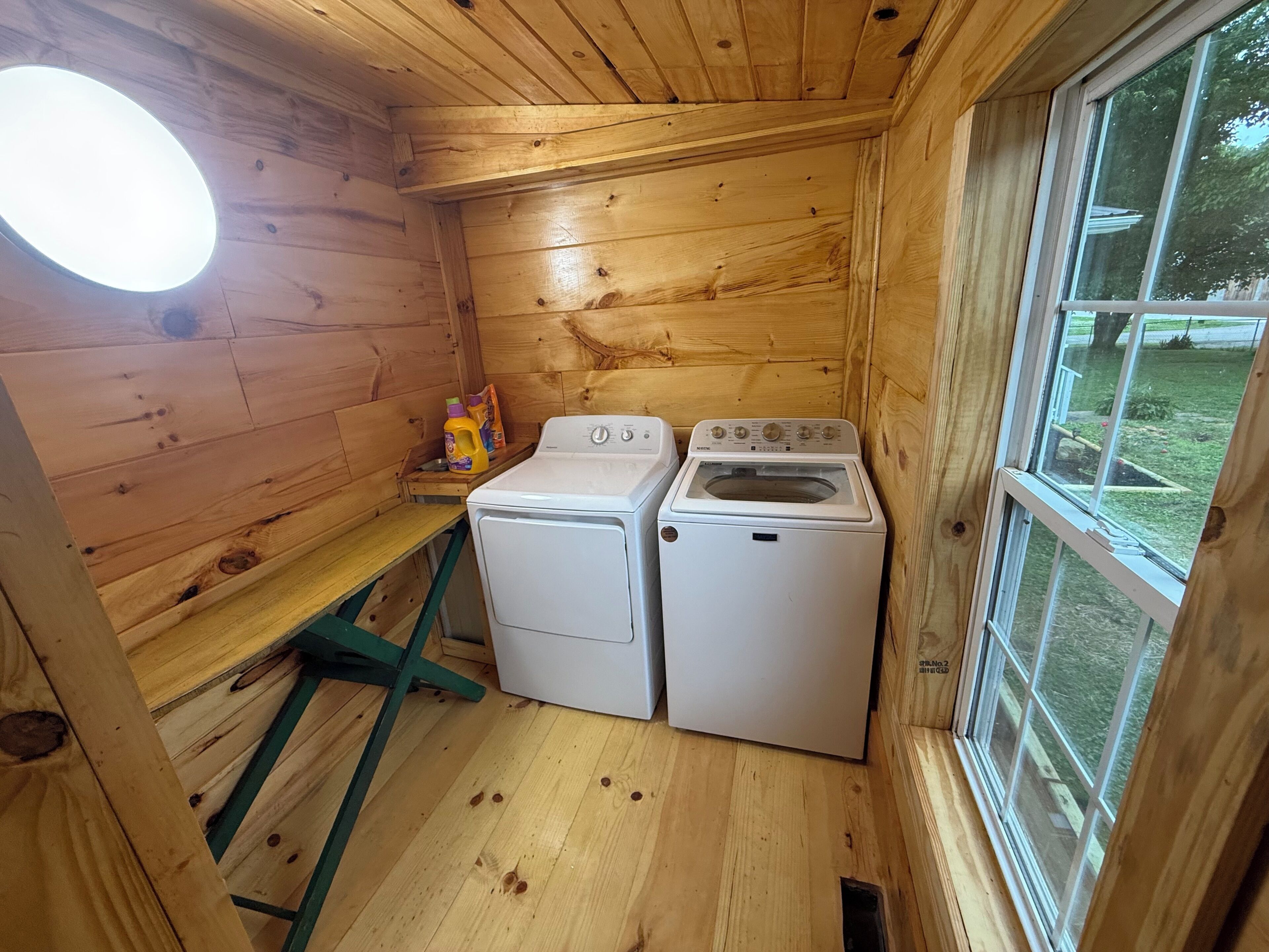 A compact wooden cabin with a washing machine, a dryer, and a small table with cleaning supplies.