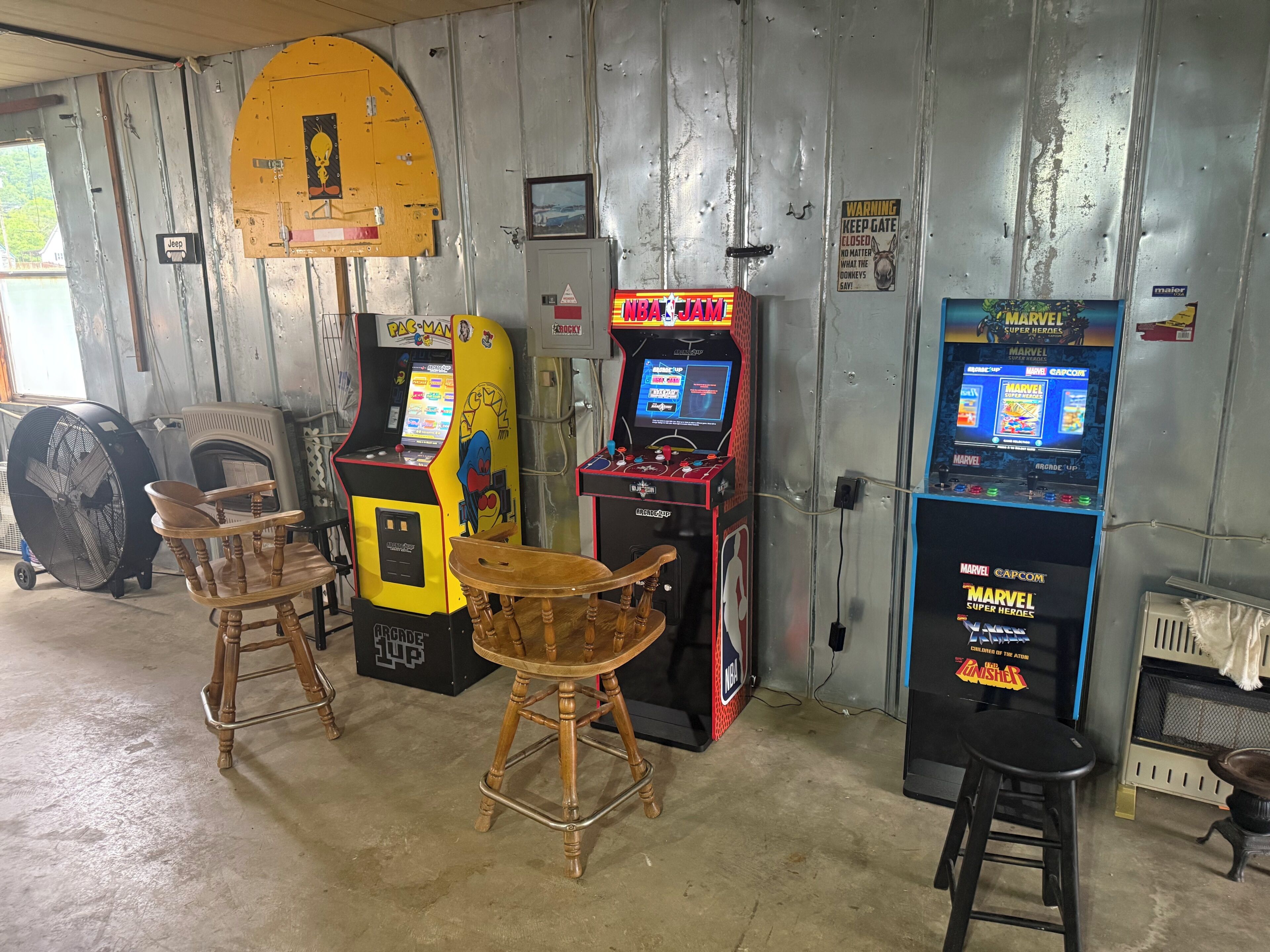 A room with arcade games, a fan, a chair, and a table.