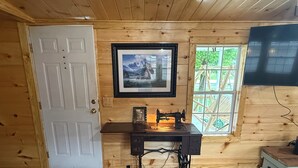 A room with wooden walls, a white door, a framed picture, a sewing machine, and a window with a view of greenery. - O-TOWN OASIS!  Near Oneida Baptist Institute & 10 miles from Manchester, KY (Oneida)